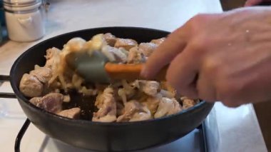Aşçı sobada soğanlı et parçaları karıştırır. Kızarmış et.