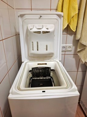 Banyoda üstü açık kapaklı bir çamaşır makinesi duruyor.