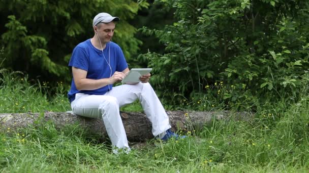 Mann sitzt auf Baumstamm und hört Musik — Stockvideo