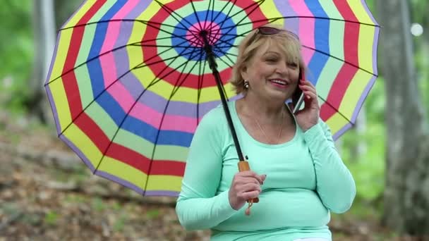 Женщина с разноцветным зонтиком разговаривает по телефону — стоковое видео