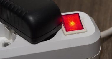 Adam taşınabilir elektrik prizinden siyah güç adaptörünü çıkarıyor ve düğmeyle elektriği kesiyor. Güç adaptörü kırmızı güç ve gösterge ile elektrikli portatif soketi çıkartır