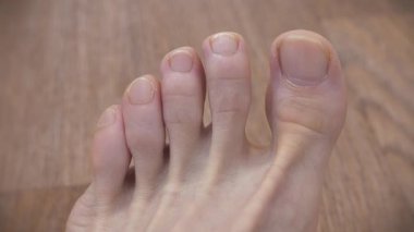 Kesilmemiş tırnakları olan bir erkek ayağı. Yetişkin bir adamın güzel ayakları ve ayak parmakları. Adam ayak parmaklarını oynatıyor.