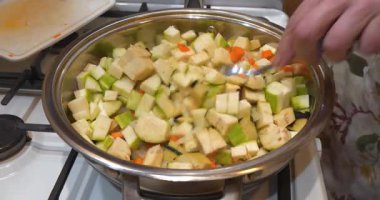 Sebze yahnisi hazırlıyorum. Aşçı bir kaşıkla sebzeleri tuzlar ve karıştırır. Sonra taze doğranmış sarı biber ekliyor. Sebze güveci fırında pişirilir. Ragout metal tavada pişiyor.