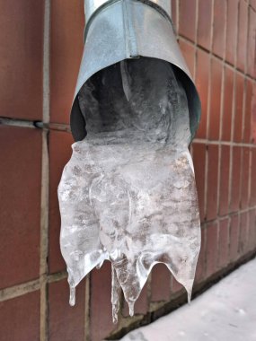 Soğuk bir hava. Yağmur suyu drenaj borusu kış boyunca dondu. Donmuş metal yağmur suyu drenaj borusu. Binanın alt kısmında buz var.