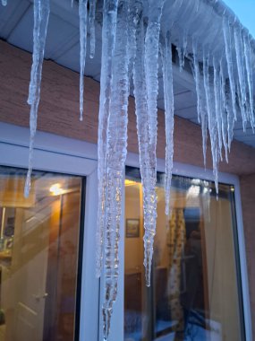 Evin çatısında büyük uzun buz sarkıtları asılı. Soğuk kış, buz oluşumu