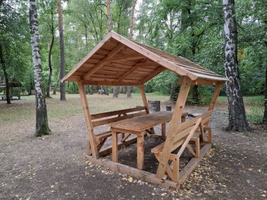 Ağaç dalları arasında bir ağaçta dinlenmek için ahşap bir çardak. Küçük bir açık hava yapısıdır ve genellikle bahçelerde veya parklarda dinlenmek için kullanılır, çatısı ve açık duvarları vardır.