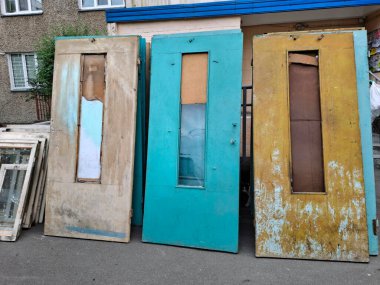 Çok katlı bir binada eski kapı ve pencerelerin tamamen değiştirilmesi. Eski ahşap kapılar apartmanın girişinin yanında duruyor. Yeni plastik pencere ve kapılarla değiştir