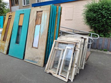 Konut evindeki eski kapı ve pencerelerin değiştirilmesi. Eski ahşap kapılar apartmanın girişinin yanında duruyor. Yeni plastik pencere ve kapılarla değiştir