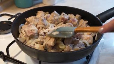 Bir aşçı, et parçalarını soğanla karıştırır. Gaz ocağında tavada kızartır.