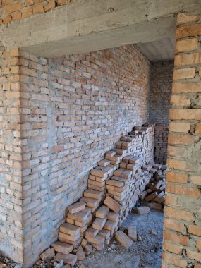 Tuğladan duvarları olan bitmemiş bir kulübenin içi. Duvarların yanına tuğlalar yığılmış. Yerleşim olmayan, tamamlanmamış bir bina.