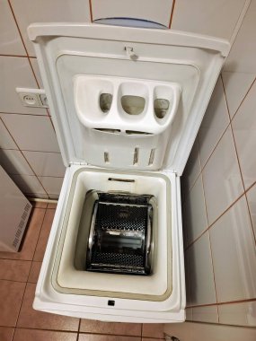 Banyoda üstü açık kapaklı bir çamaşır makinesi duruyor.