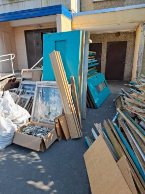 Çok katlı bir binadaki eski Sovyet kapı ve pencerelerinin tamamen değişmesi. Eski ahşap kapılar apartmanın girişinin yanında duruyor. Yeni plastik pencere ve kapılarla değiştir