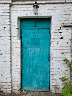 Eski mavi, ahşap, kapalı bir kapı. Kapının etrafında tuğla duvarlar beyaza boyanmış.