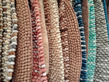Multicolored carpets on a store counter. There are small soft rugs hanging in the shop window. Soft bathroom floor mats are sold in the supermarket