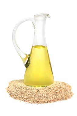 Cam sürahide susam yağı ve beyaz arka planda susam tohumu.