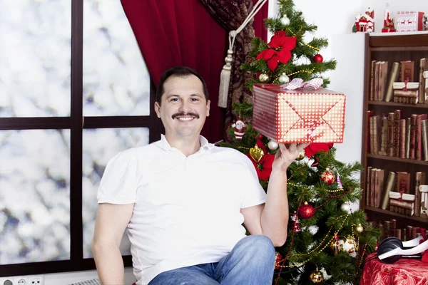 Happy man with gift near a christmas tree — Stock Photo, Image