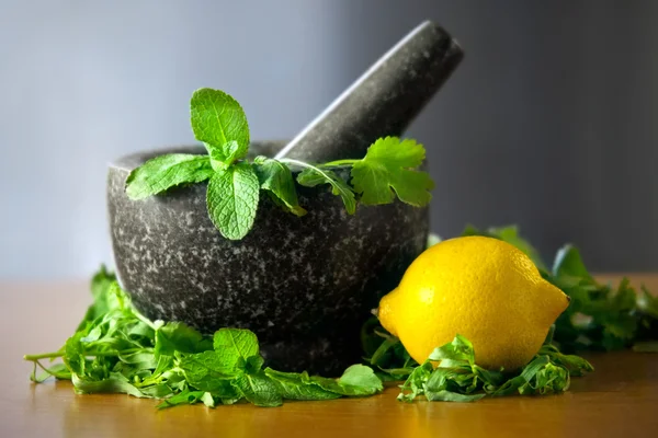 Selezione di foglie di erbe in un mortaio di granito con pestello con limone — Foto Stock