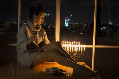 Kutlama Hanukkah menorah ile cam kenarında oturan bir kız.