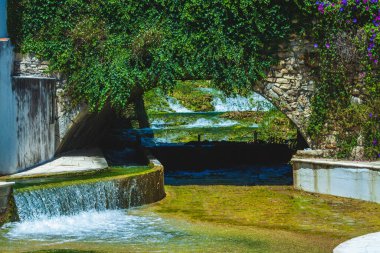 Altında bir nehir ve küçük bir şelale olan yosun kaplı eski bir köprü.