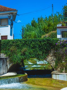 Altında bir nehir ve küçük bir şelale olan yosun kaplı eski bir köprü.