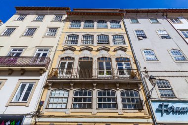 Düşük açılı bir çekim, renkli, yıpranmış, tarihi binaların ön cephelerini, süslü balkonları ve şebeke pencereleriyle canlı mavi gökyüzüne yansıtıyor.