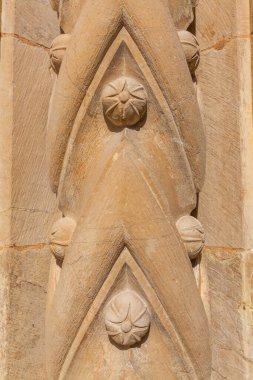 A close-up of a weathered stone architectural detail features repeating pointed arches and carved floral rosettes, showcasing the intricate craftsmanship of historic masonry