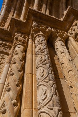 A close-up view of ornate, sunlit stone columns showcases intricate carvings of leaves and geometric patterns, highlighting the masterful craftsmanship of historic architecture.