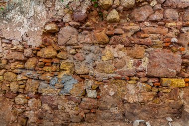 A close-up of a weathered, rustic stone wall showcases a rich tapestry of textures and earthy tones, with crumbling plaster revealing layers of history.