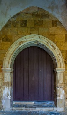 Tarihi bir binanın eski cephesine kurulmuş eskimiş, siyah ahşap kapılı, kavisli taş bir kapı.