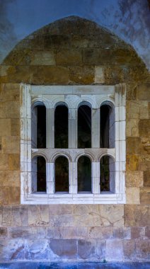 Süslü, çok kemerli taştan bir pencere, beyaz bir iz sürme seti, yıpranmış, altın renkli bir taş duvar, yuvarlak kemerin altında.