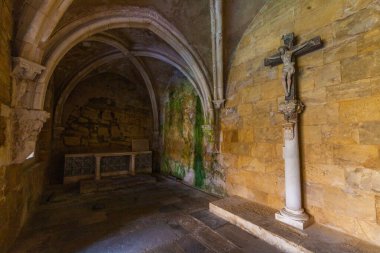 Loş, tarihi bir kilisede bir sütun üzerinde haç ve kemerlerin altında, antik duvarlarda yosun lekeleri olan bir sunak bulunur..