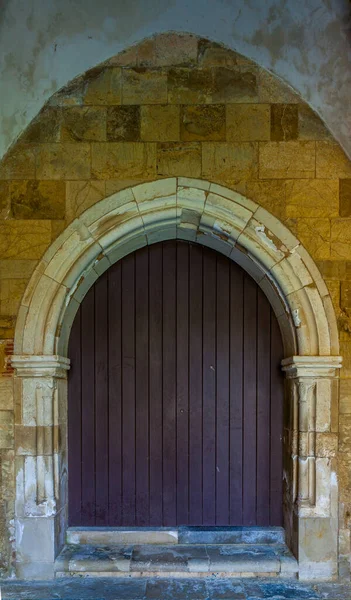 Tarihi bir binanın eski cephesine kurulmuş eskimiş, siyah ahşap kapılı, kavisli taş bir kapı.