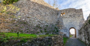 Leiria. Kavisli geçit ve dar kaldırım taşı yolu olan antik taş güçlendirme duvarı kısmen çimen ve çalılarla kaplı parçalı bulutlu bir gökyüzü altında