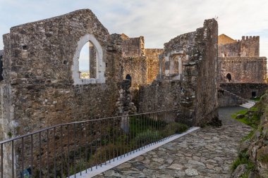 Leiria. Zarif kemerli pencereleri olan antik taş kalıntıların manzarası, dolambaçlı kaldırım yolu, ve modern parmaklıklar, hepsi bulutlu bir gökyüzüne karşı sıcak günbatımı ışığında yıkanmış