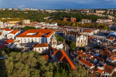Leiria. Geniş bir hava manzarası, ikonik kırmızı kiremitli çatıları, beyaz yıkanmış binaları ve çarpıcı ve bulutlu gökyüzünün altında yemyeşil tepeler arasında yuva yapmış seçkin bir kilisesi olan tarihi bir Avrupa kasabasını yakalıyor..