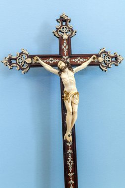 Biscainhos Müzesi. - Braga. Karmaşık bir şekilde işlenmiş bir haç, koyu renk ahşap bir haçta bulunan ve flütlü bir temele yerleştirilmiş, melek motifli, dingin mavi bir duvara dayanmış, İsa 'nın ayrıntılı bir fildişi figürünü içerir..