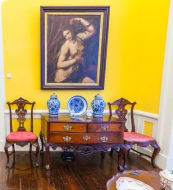 Biscainhos Müzesi. - Braga. İçinde canlı sarı duvarlar olan tarihi bir oda. Çerçevelenmiş barok yağlı bir resim var. Yarı çıplak bir kadın figürü. Yılanlı kumaşı ve kolu tutuyor.