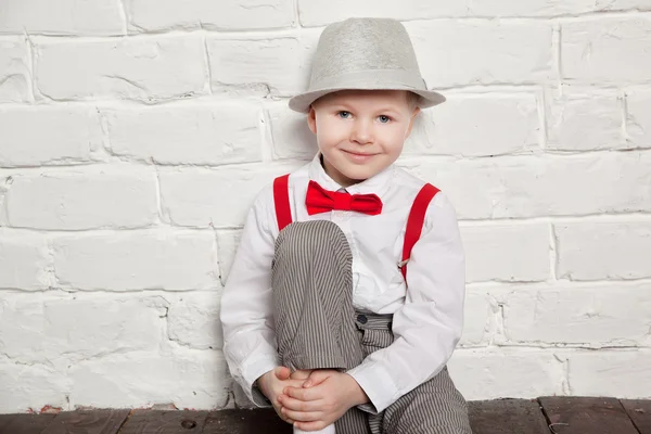Bambino che indossa un papillon rosso, bretelle e camicia bianca contro un muro di mattoni bianchi . — Foto Stock