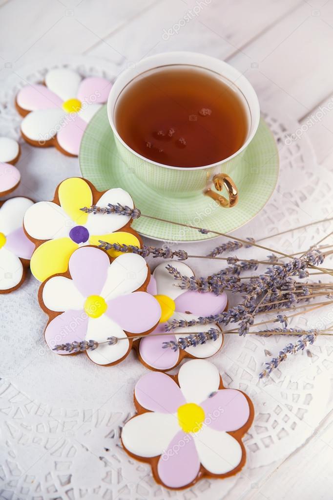 Cup of tea, handmade cookies like flowers on white wooden table.