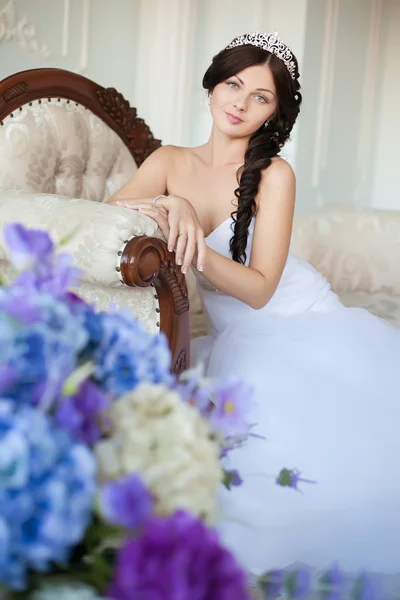 Young beautiful bride sits on an elegant sofa and looking at the camera — Stock Photo, Image