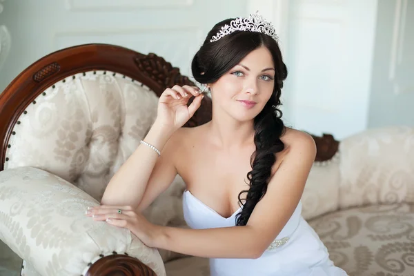 Young beautiful bride sits on an elegant sofa and looking at the camera — Stock Photo, Image