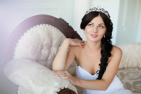 Молодая красивая невеста сидит на элегантном диване и смотрит в камеру — стоковое фото