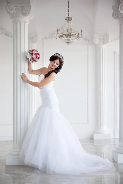 Όμορφη μελαχρινή νύφη ένα νυφικό και ένα στέμμα στο κεφάλι, πλήρους μήκους πορτραίτο της. Εσωτερικό με στήλες. — Φωτογραφία Αρχείου