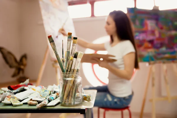 Artista feminina trabalhando na pintura em estúdio. Imagem de fundo, foco seletivo em primeiro plano — Fotografia de Stock