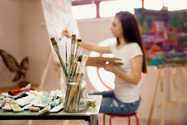 Female Artist Working On Painting In Studio. Background image, selective focus on  foreground