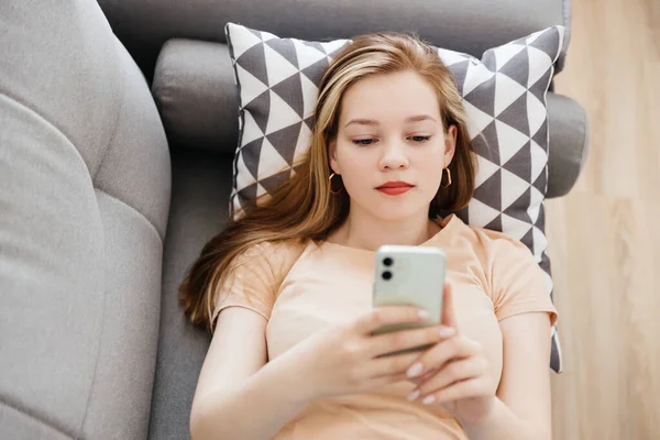 Primer plano de una chica relajada usando un teléfono inteligente acostado en un sofá — Foto de Stock
