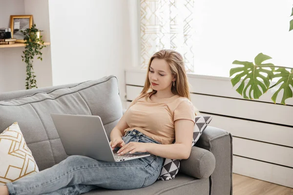 Молода жінка використовує ноутбук, сидячи на дивані — стокове фото