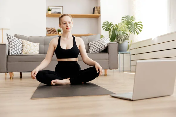 Молода приваблива жінка практикує йогу вдома і використовує ноутбук, йогу для початківців онлайн — стокове фото