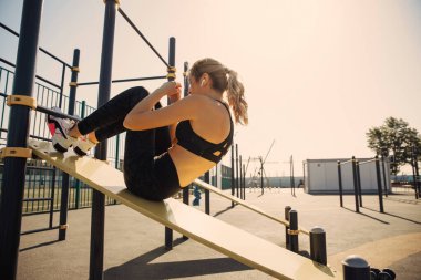 Açık hava idman istasyonunda karın kası egzersizi yapan narin genç bir kadın..