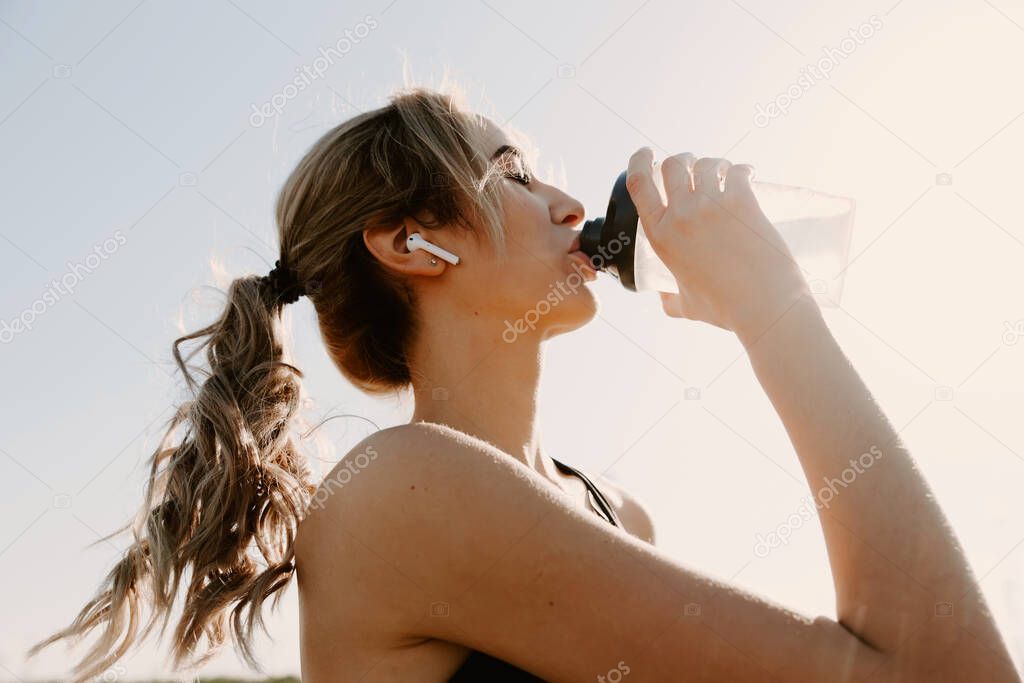 Athletic woman using earphones and drinking water
